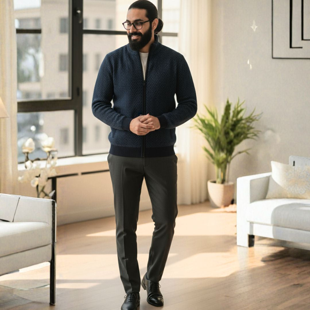 Man in a navy sweater and gray pants standing in a modern living room.