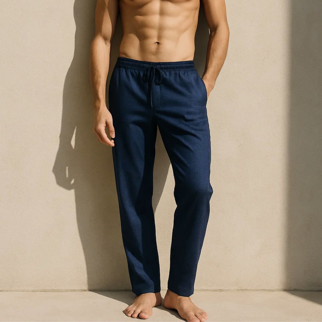 Man wearing navy blue pajama pants against a beige wall.