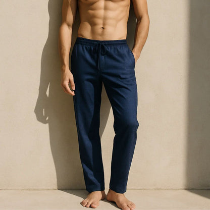 Man wearing navy blue pajama pants against a beige wall.