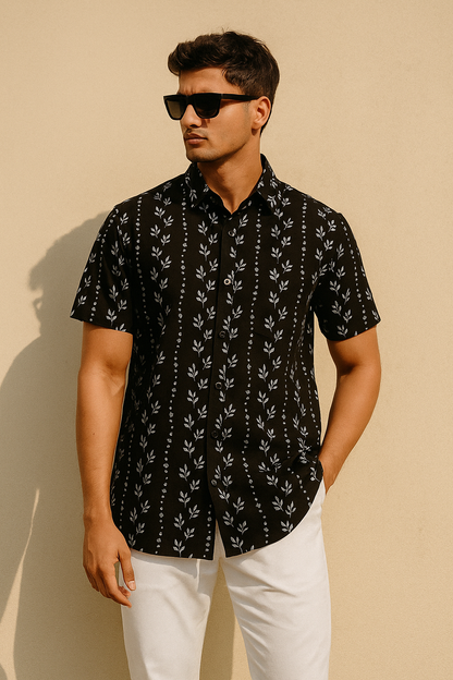 Man wearing a black patterned shirt and white pants against a beige background